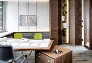 Ein modernes Büro mit einem großen Tisch und bequemen Stühlen. Die Wände sind in hellen Holz- und Grautönen gehalten, und es gibt viel natürliches Licht.