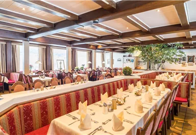 Ein gemütliches Restaurant mit eleganten Tischen und roten Bänken. Das Licht strömt durch große Fenster und sorgt für eine einladende Atmosphäre.