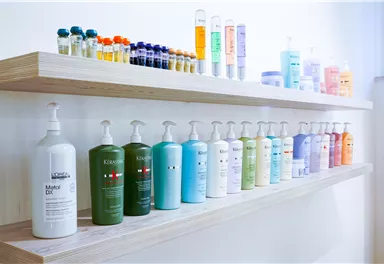 Eine Reihe von Haarpflegeprodukten in verschiedenen Farben auf einem Holzregal. Die Flaschen sind ordentlich angeordnet und zeigen eine Vielfalt an Marken und Formulierungen.