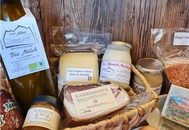 A basket full of regional foods, including milk, cheese, jam, and eggs. The products are attractively packaged and surrounded by wood grain.