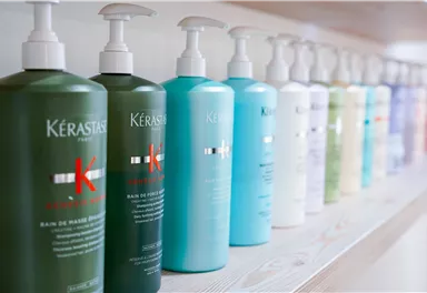 Eine Reihe von Kérastase Haarpflegeprodukten in verschiedenen Farben. Die Flaschen stehen ordentlich auf einem Regal.