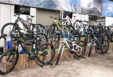 Ein Fahrradgeschäft mit mehreren Mountainbikes auf einem Präsentationsstand. Die Bikes sind in verschiedenen Farben und Designs ausgestellt.