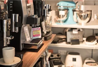 A modern kitchen setup with various appliances like coffee machines and food processors. Several household devices are lined up on a wooden shelf.