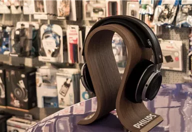 A stylish pair of headphones stands on a wooden stand. In the background, various electronic accessories are visible.