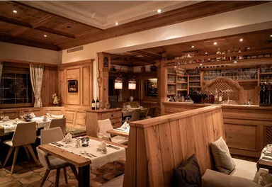Ein gemütliches Restaurant mit Holzinterieur und sanfter Beleuchtung. Tische sind liebevoll gedeckt und eine Bar im Hintergrund ist sichtbar.