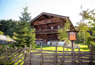 A cozy wooden house with a spacious garden and green trees. In the foreground, there is a fence made of wooden rails.