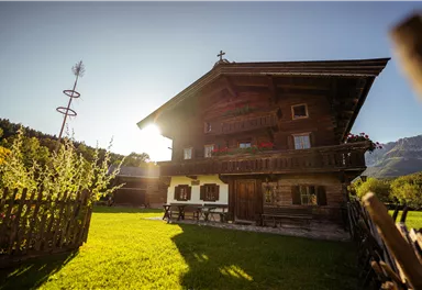 A traditional wooden house with a balcony in a beautiful landscape. In the background, mountains and a clear sky are visible.