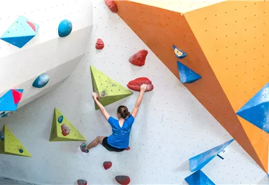A person climbing a colorful climbing wall. The wall has various holds in blue, red, and green colors.