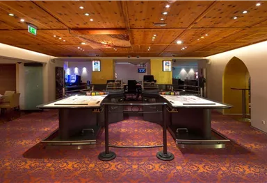 An elegant casino with a central gaming table and a stylish, warm wooden ceiling. The atmosphere is inviting and luxurious.