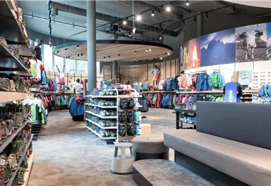 Ein moderner Sportladen mit Regalen voller Outdoor-Bekleidung und -Schuhen. Die helle und großzügige Gestaltung lädt zum Stöbern ein.