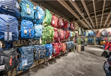 Ein Fachgeschäft mit einer großen Auswahl an Rucksäcken in verschiedenen Farben. Die Rucksäcke sind ordentlich an Wänden aufgehängt.