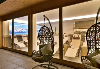 A modern relaxation area with hanging chairs and loungers. Large windows offer a view of the mountains and create a calm atmosphere.