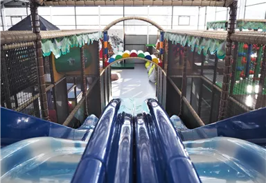 A slide in an indoor playground with colorful decorations. The view from the slide shows the play areas in the background.