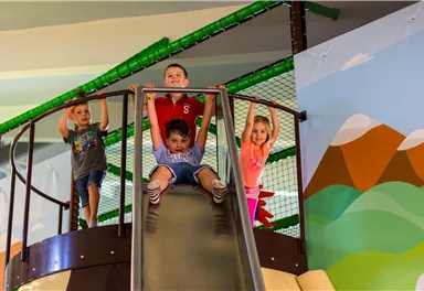 A group of four children is playing in an indoor play area. They are standing on a slide and are having a lot of fun.