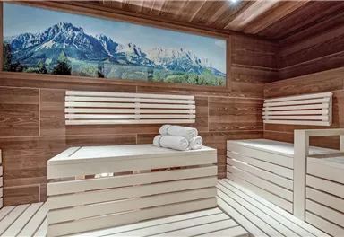 A modern sauna room with wooden benches and fresh towels. A large picture of mountains and green landscape adorns the wall.