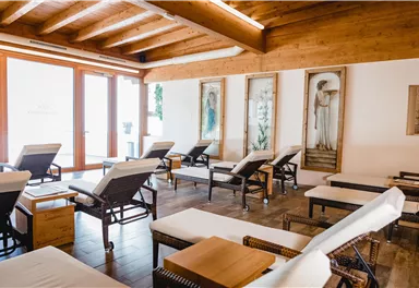 A quiet room with comfortable loungers and wooden walls. Daylight streams in through large windows, and there are artworks visible on the walls.