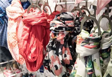 Eine Auswahl an bunten Schals hängt an einem Kleiderständer. Die Schals haben verschiedene Designs und Farben.