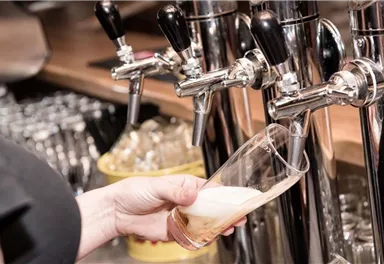A person is pouring a beer from a tap. In the background, glasses and the bar are visible.
