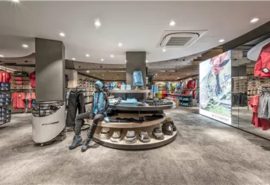 Ein moderner Sportartikelgeschäft mit bunten Kleidungsteilen und Ausrüstung. Im Mittelpunkt steht ein runder Tisch mit Sportschuhen und Bekleidung.