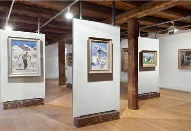 An art museum with several picture frames on white walls. The room has wooden floors and a warm atmosphere.