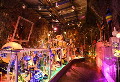 Ein bunter Raum mit künstlerischen Glasskulpturen und farbigem Licht. Die Wände sind aus Felsen, was eine einzigartige Atmosphäre schafft.