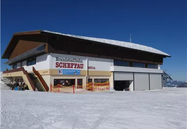 Ein Gebäude der Bergbahn Scheffau in einer schneebedeckten Umgebung. Der Himmel ist klar und die Winterlandschaft ist malerisch.