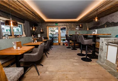 A modern restaurant with wooden floors and cozy seating. Large windows offer a view outside to a tree.