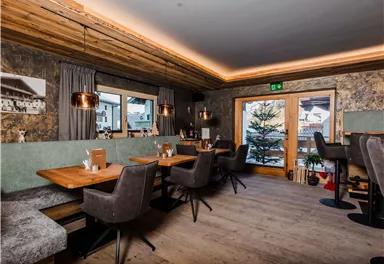 A modern restaurant with a wooden ceiling and cozy seating areas. The windows offer a view of the outdoor terrace and the soft lighting creates an inviting atmosphere.