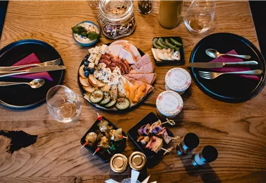 A beautifully set table with a selection of cheese, sausage, and fresh fruit. There are also glasses and cutlery ready for a convivial meal.