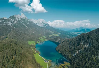 A picturesque mountain lake surrounded by green forests and majestic mountains. The sky is clear with a few clouds.