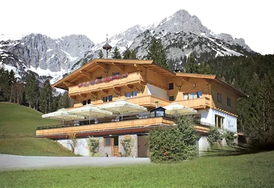 A charming wooden house surrounded by green meadows and majestic mountains. Snow-capped peaks are visible in the background.