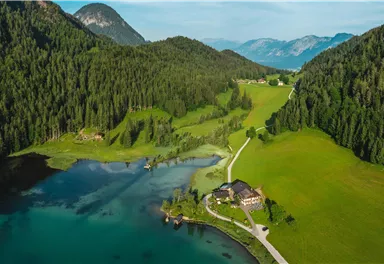 Eine malerische Landschaft mit einem klaren See und üppigen grünen Wiesen. Im Hintergrund erheben sich sanfte Hügel und Berge.