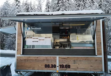 A wooden food stall in a snowy landscape. The opening hours are from 08:30 to 19:00.