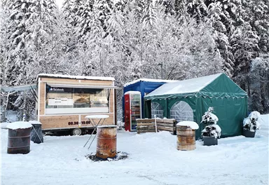 A sales booth and a tent are set up in a snowy winter landscape. In the background, snow-covered trees can be seen.