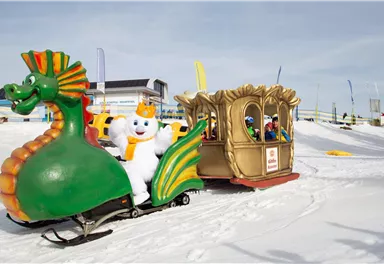 Ein bunter Schlitten in Form eines Drachen fährt durch den Schnee. Ein fröhlicher Schneemann sitzt in der goldenen Karosse des Schlittens.