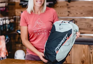 Two people are standing in front of a store with outdoor gear. In the background, there are advertising banners and sales booths visible.