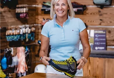 A store with a variety of shoes and backpacks.
Shelves are filled with sports items, and the floor is carpeted.