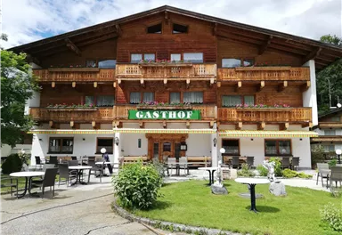 A cozy inn with a wooden facade and balconies. The outdoor area features tables and chairs in a green environment.