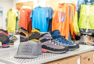 A selection of hiking shoes and outdoor clothing is displayed on a presentation table. In the foreground, there is a gray hat.