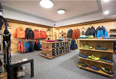 A sports store with a selection of outdoor clothing and shoes. The walls are adorned with jackets and pants, and shelves display various shoes.