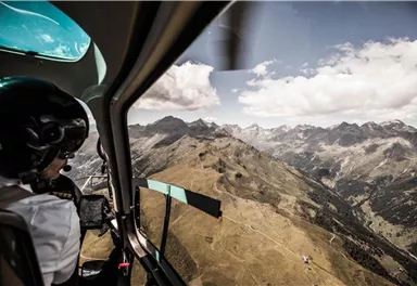 A view from the helicopter window of majestic mountains and a picturesque landscape. A pilot controls the aircraft over the alpine surroundings.