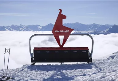 A ski lift station with a distinctive sign in the shape of a llama. In the background, snow-covered mountains and a sea of clouds can be seen.