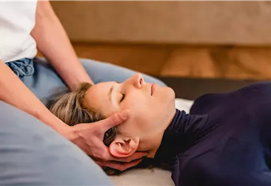 A relaxation massage is performed on a person who is lying relaxed on a massage table. The hands of the massage therapist are on the person's head.