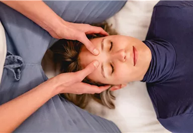 A woman receives a relaxing head massage. She lies quietly with her eyes closed while someone gently holds her head.