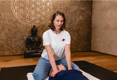 A woman is giving a massage in a quiet room. In the background, there is a Buddha statue and a geometric wall design.