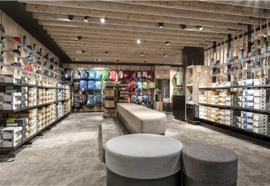 Ein modernes Geschäft mit einer Vielzahl von Rucksäcken und Schuhen. Helle Regale und ein einladendes Design schaffen eine freundliche Einkaufsatmosphäre.