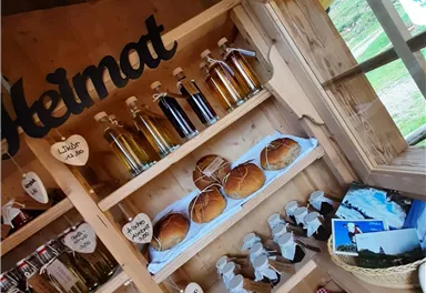 A wooden shelf full of homemade products, including bottles with various liquids and freshly baked rolls. The room exudes a welcoming, rustic atmosphere.