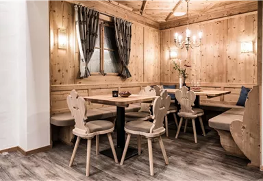 Ein gemütliches Esszimmer mit Holzwänden und einem modernen Tisch. Es gibt mehrere Stühle und eine Sitzbank, umgeben von stilvollen Vorhängen.