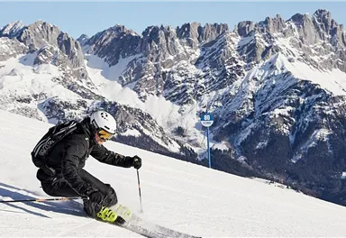 A skier is going down the snowy slope. In the background, impressive, snow-covered mountains can be seen.