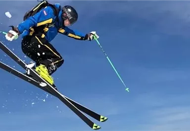 Ein Skifahrer springt durch die Luft und macht einen Trick. Der Himmel ist klar und blau.